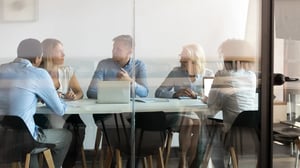 Mitarbeitende sitzen gemeinsam in einem Besprechungsraum und sprechen an einem Konferenztisch über Unternehmens- und Compliance-Themen.
