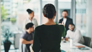 Eine Person delegiert Aufgaben an ein Team in einem modernen Besprechungsraum.