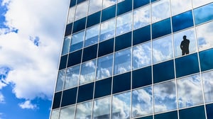 In einem Fenster eines modernen Bürogebäudes steht die Silhouette einer Person und blickt nach draußen.