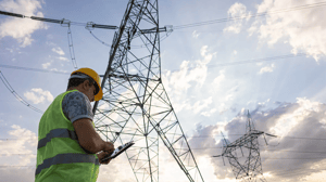 Ein Techniker mit Schutzweste und Helm inspiziert Strommasten.