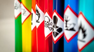 Farbige Chemikalienbehälter mit Gefahrensymbolen für verschiedene chemische Gefahren und Stoffeigenschaften.
