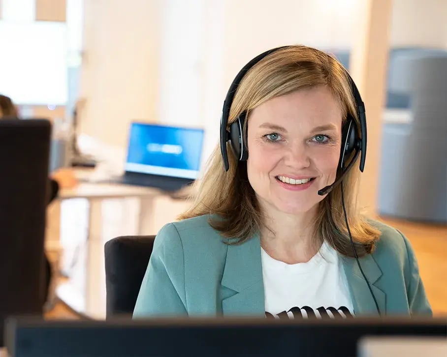 Freundliche Frau mit Headset, lächelnd vor dem Bildschirm im Büro