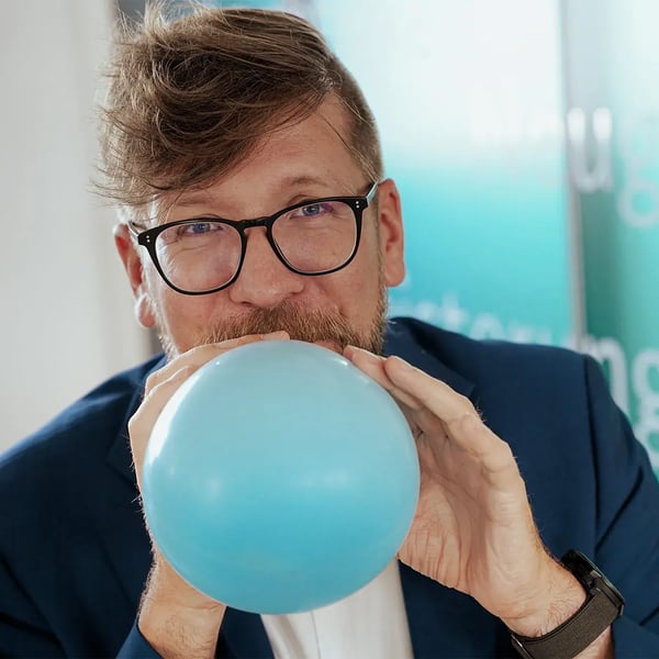 Person bläst Luftballon auf und blickt in die Kamera Person bläst Luftballon auf und blickt in die Kamera
