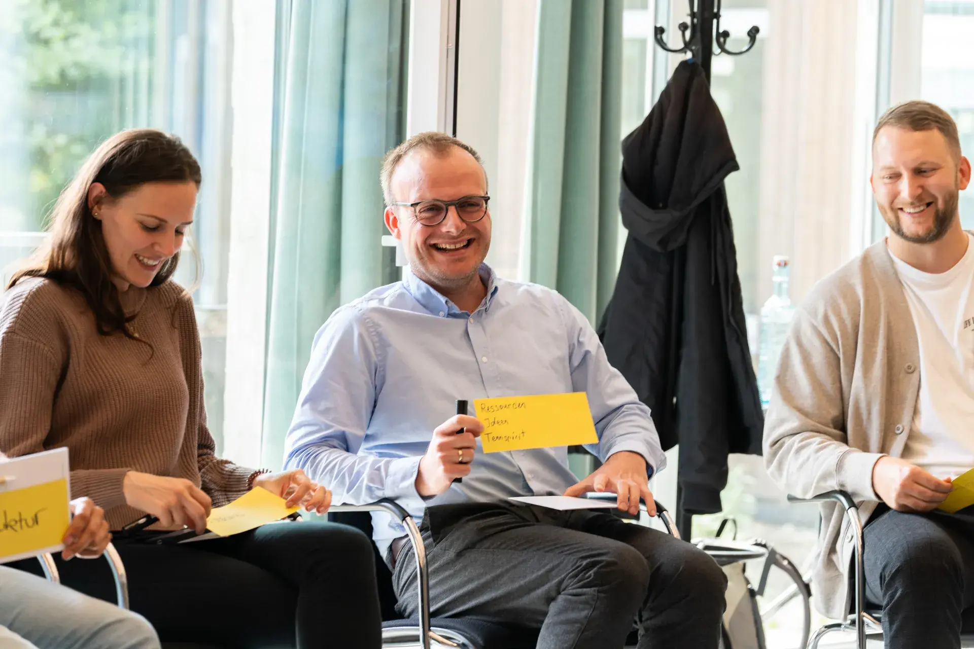 Drei Personen beim Eticor Focus Day im Stuhlkreis, lachend beim Ausfüllen ihrer Moderationskarten Drei Personen beim Eticor Focus Day im Stuhlkreis, lachend beim Ausfüllen ihrer Moderationskarten