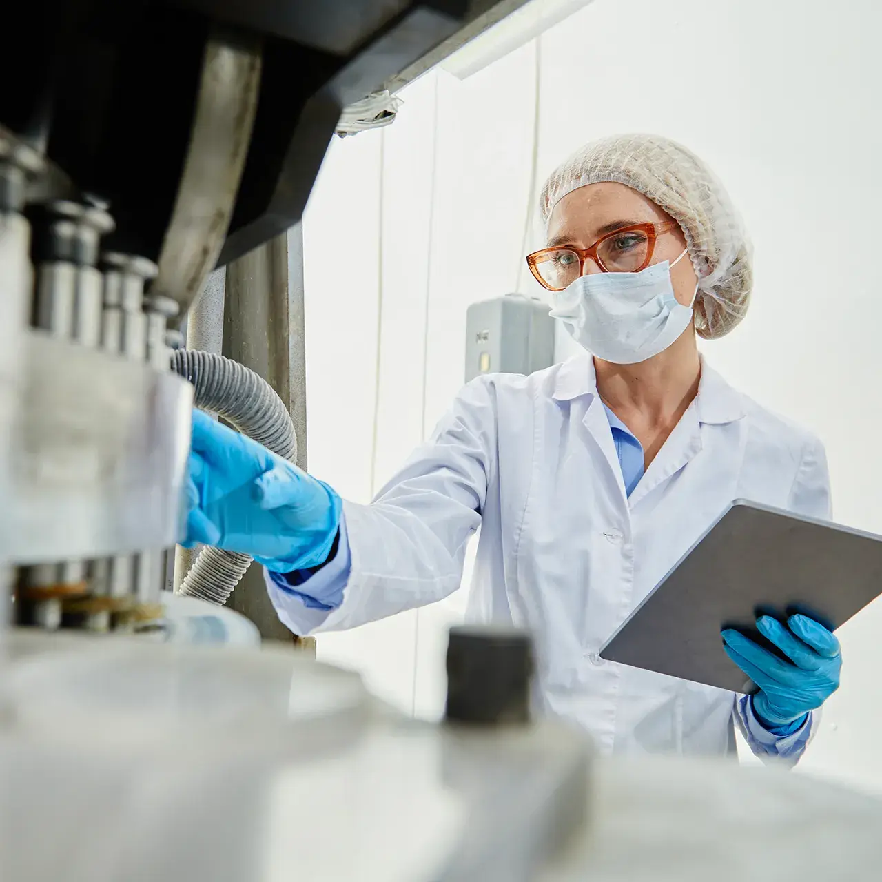 Eine Laborfachkraft mit Schutzkleidung und Tablet überprüft eine Produktionsanlage in einem Reinraum.