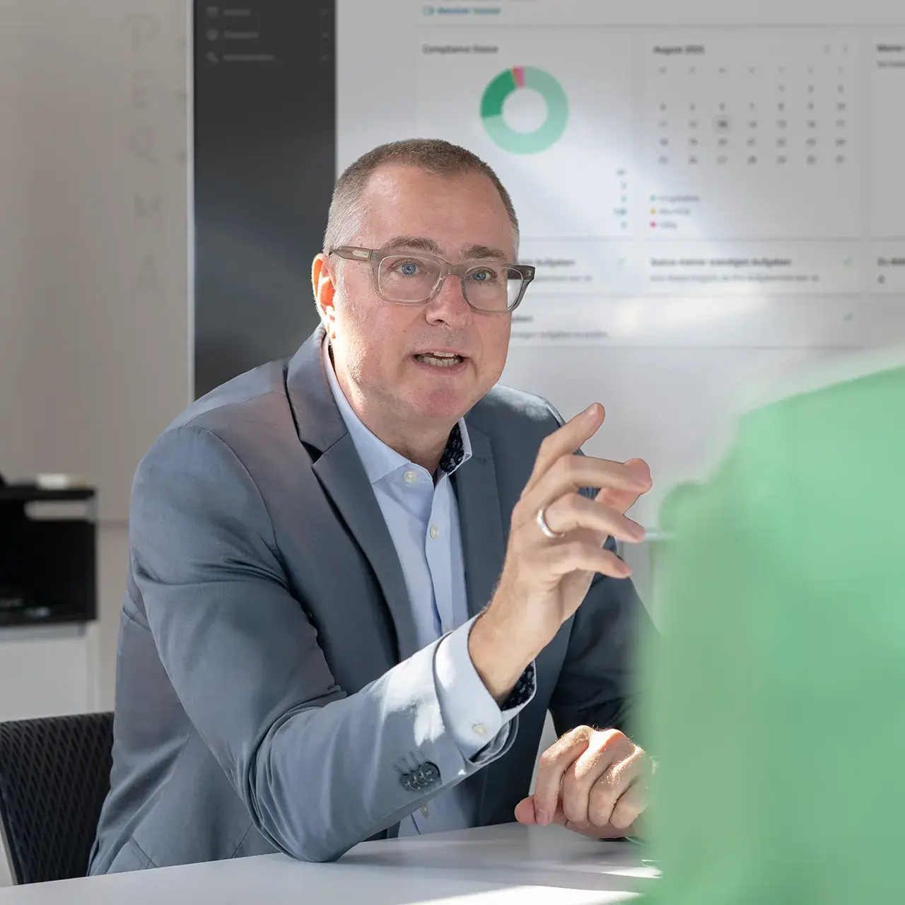 Mann spricht in einem Meeting, im Hintergrund ist das Dashboard der Eticor Compliance Management Software sichtbar.